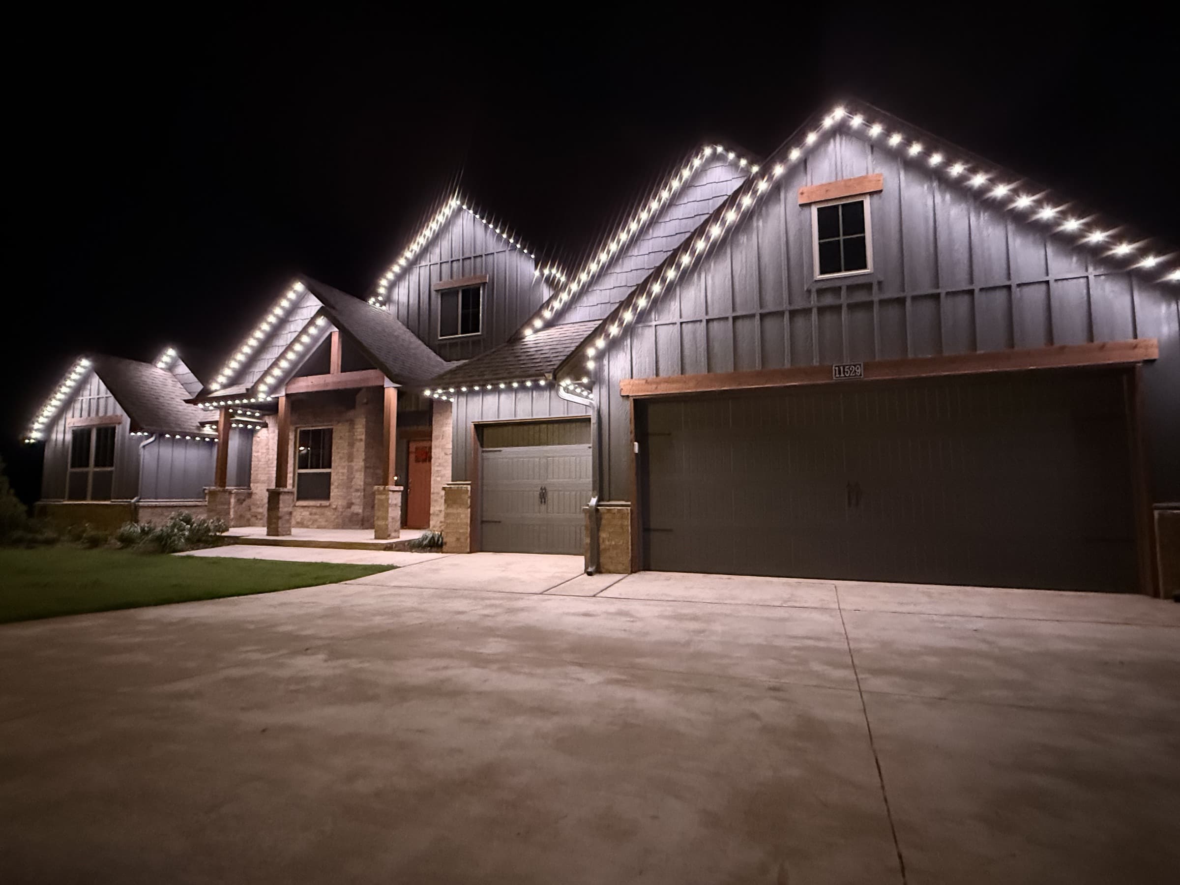 Multi-gable mixed-material home with TruLight permanent lighting set to a warm-white roofline effect.