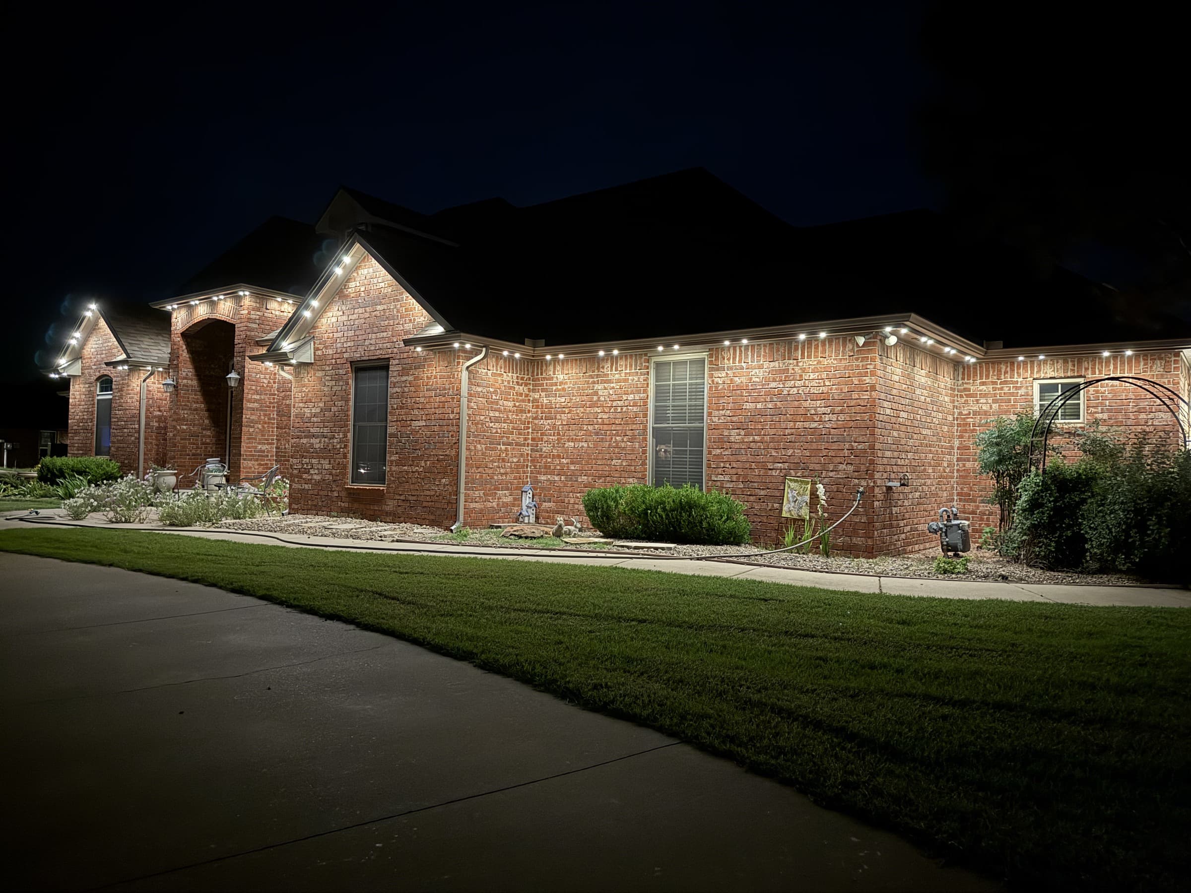 Single-story brick home with long eaves and TruLight permanent lighting set to a warm-white roofline effect.