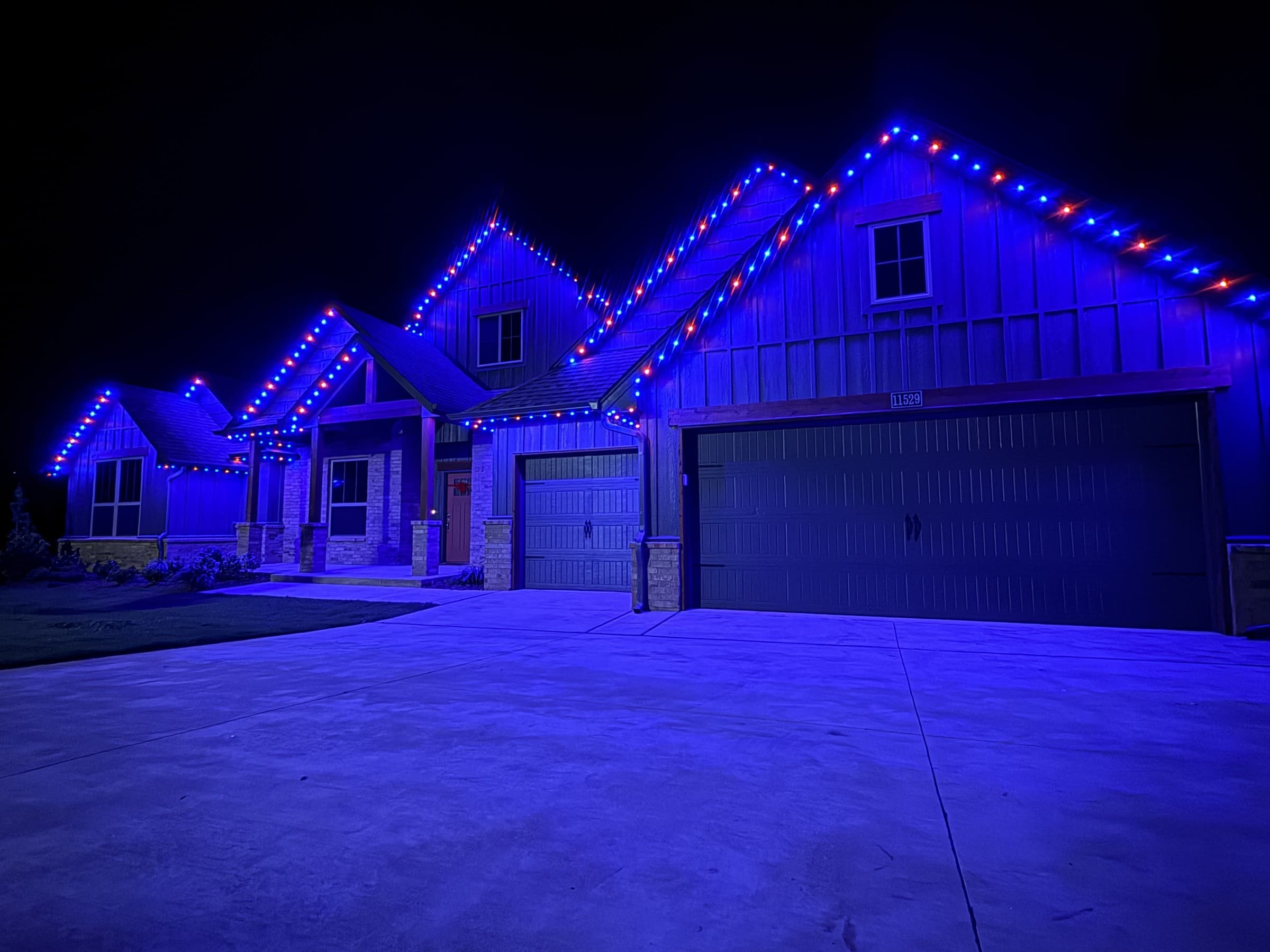 Multi-gable mixed-material home with TruLight permanent lighting set to a blue roofline effect.