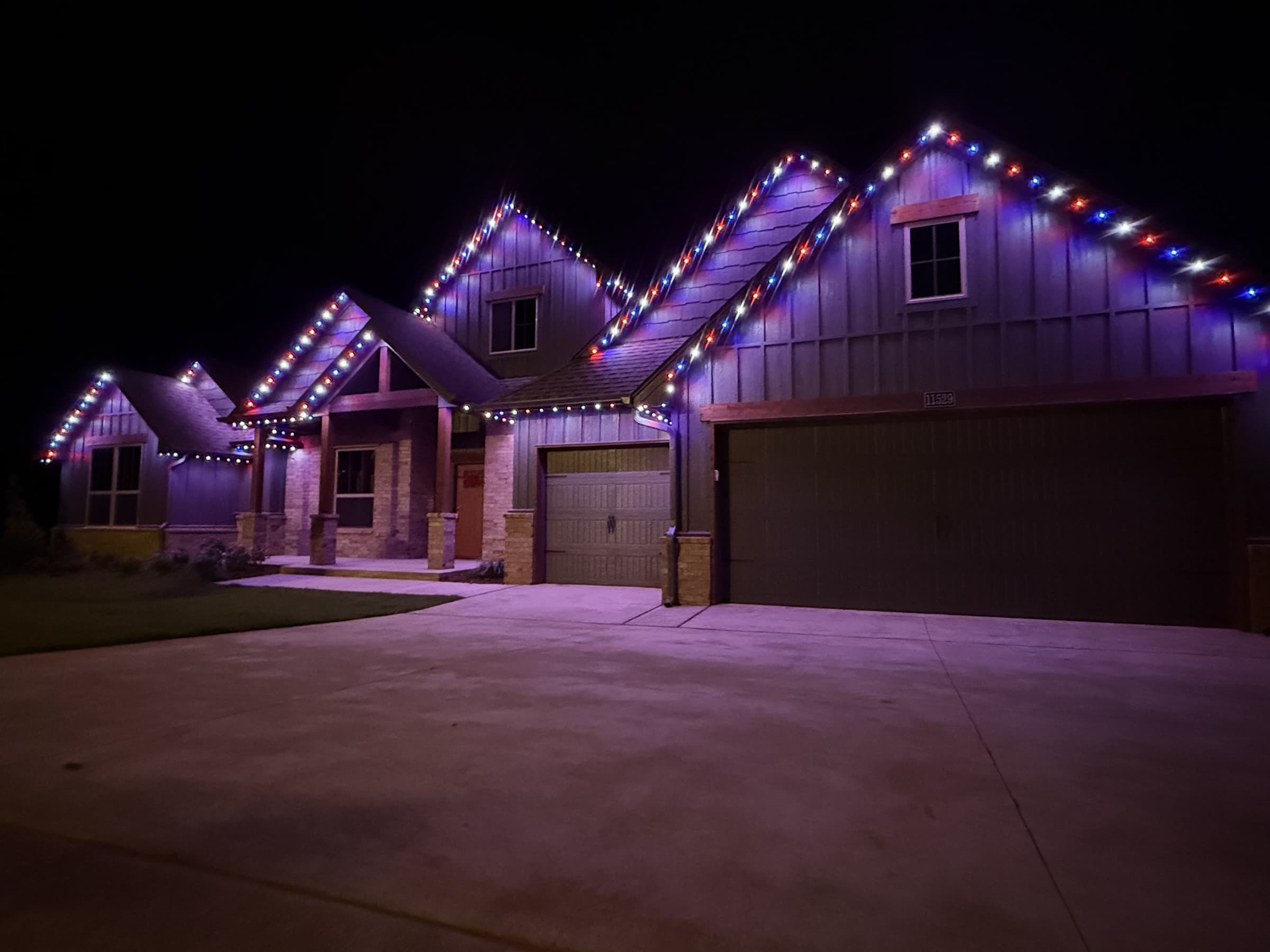 Multi-gable mixed-material home with TruLight permanent lighting set to a red, white and blue multicolor roofline effect.