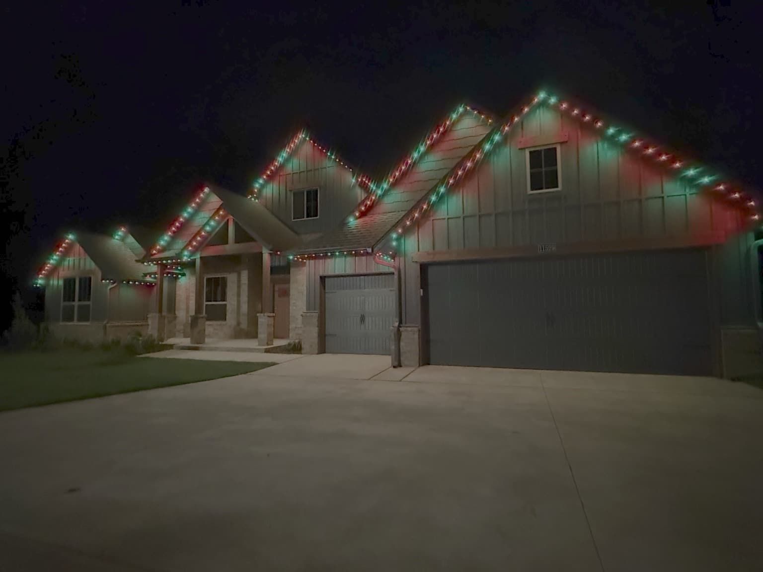 Multi-gable light-sided home with red-and-green permanent roofline lights creating a Christmas lighting effect.
