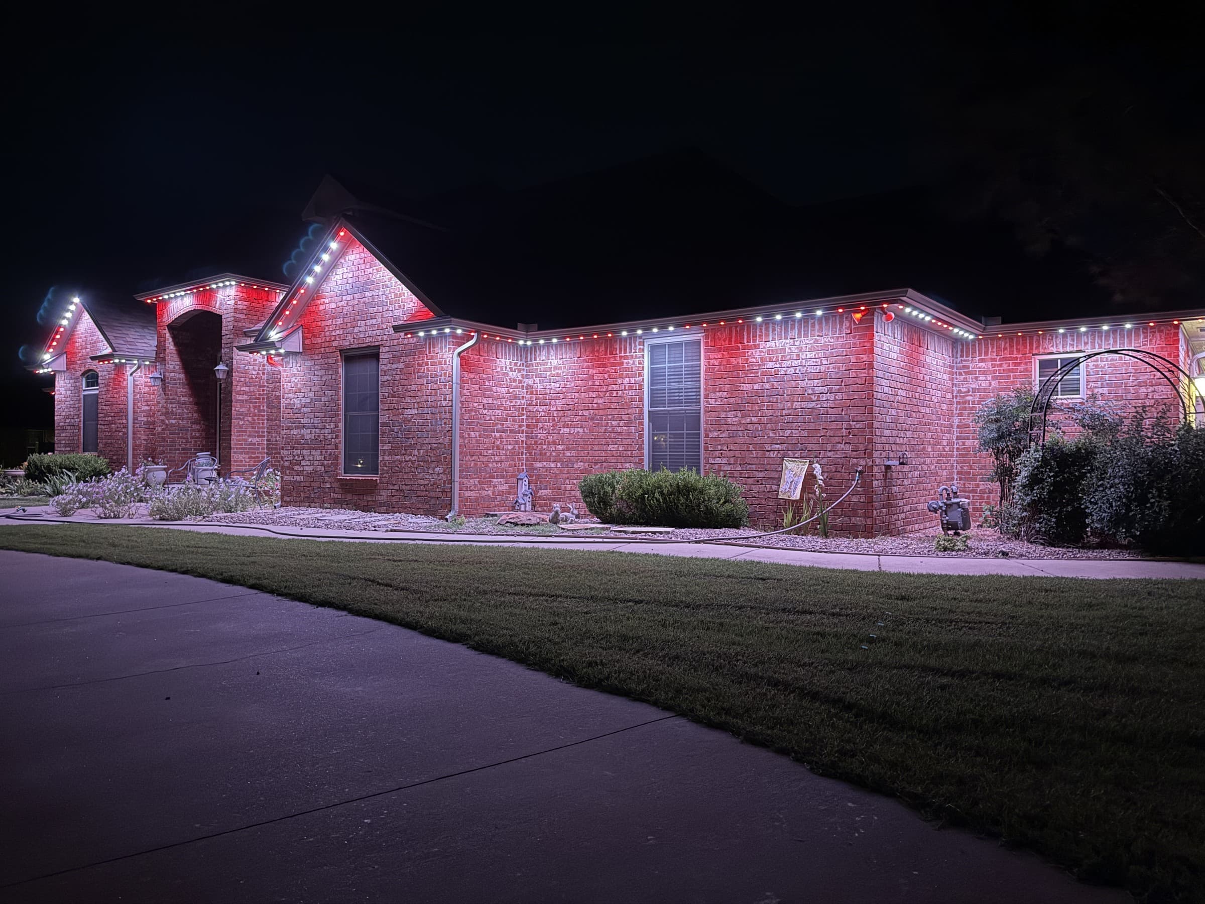 Single-story brick home with long eaves and TruLight permanent lighting set to a red-and-white roofline effect.