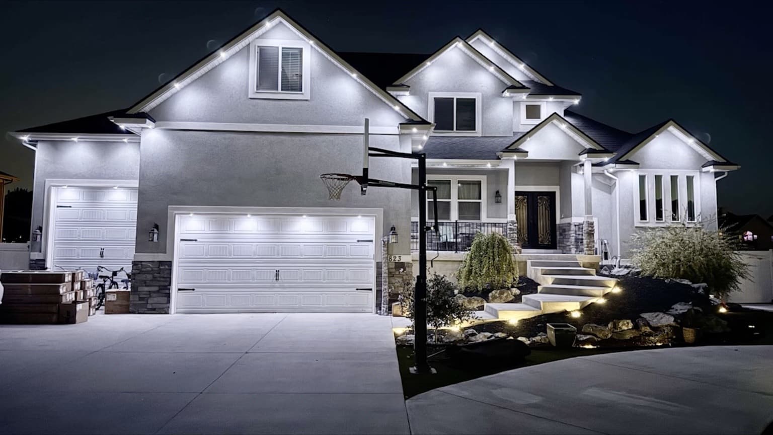 Two-story stucco home with stone accents and bright white permanent lights outlining several front-facing gables.