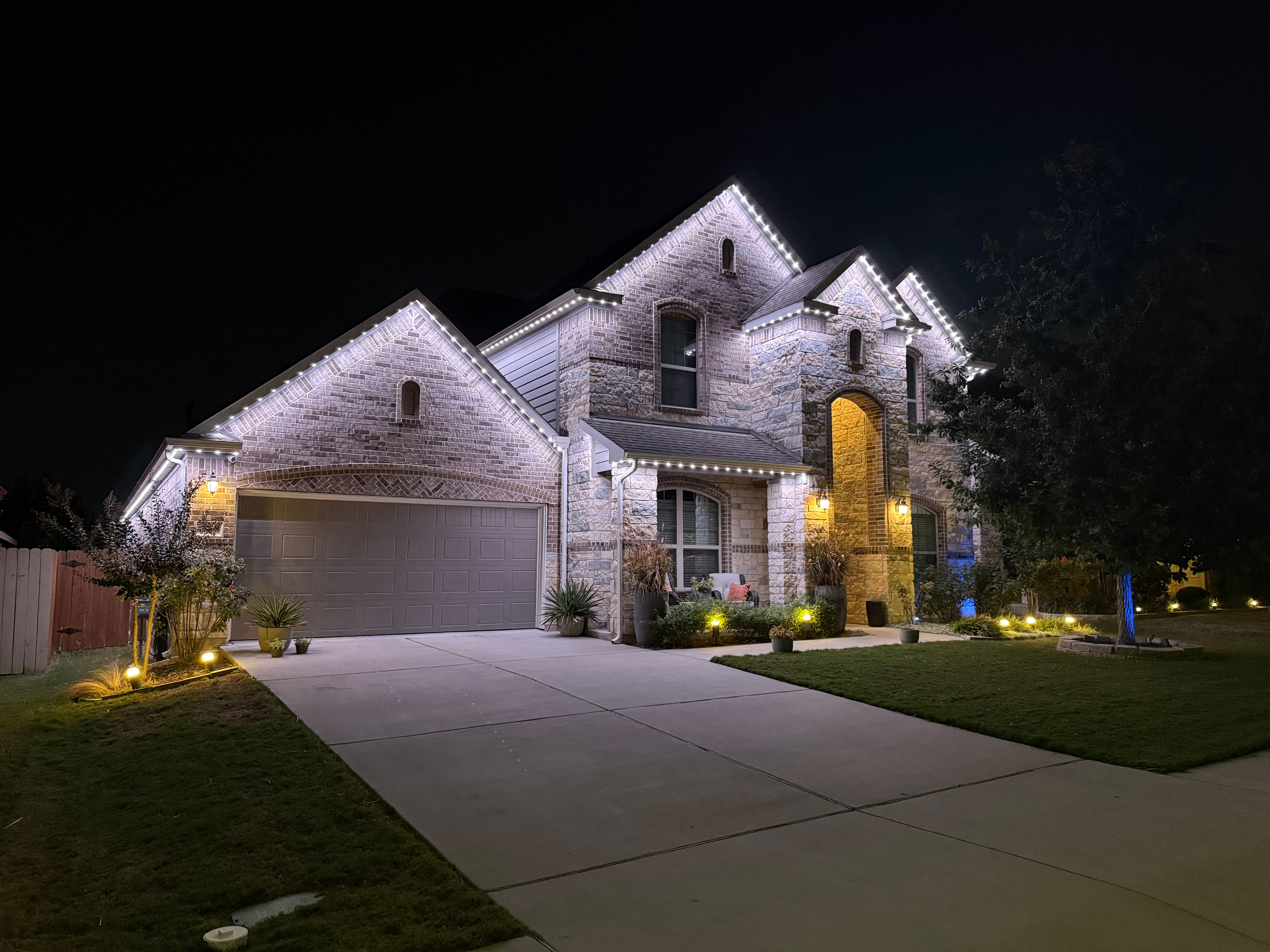 TruLight manufacturer example: stone home with white permanent roofline lighting at night